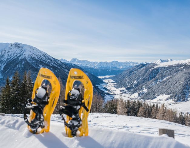 Zwei gelbe Schneeschuhe im Schnee mit Blick ins verschneite Gsieser Tal und umliegende Berge.