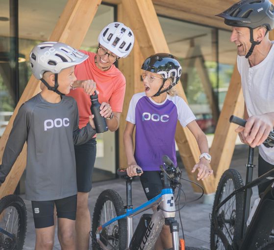 Lachende Familie mit Fahrrädern macht eine Trinkpause beim Radfahren in den Bergen.